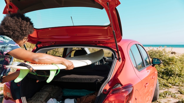 Young black male getting surfboard out of trunk by seacoast