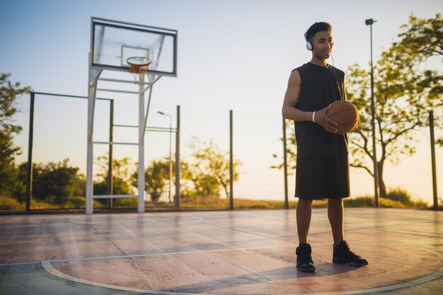 Young black man doing sports, playing basketball on sunrise, listening to music on headphones, active lifestyle, summer morning