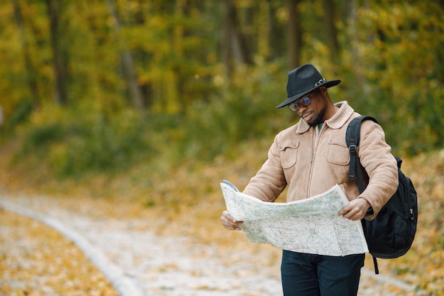 Young black man hitchhiking on road and looking at map. Male traveler feeling lost, traveling alone by autostop