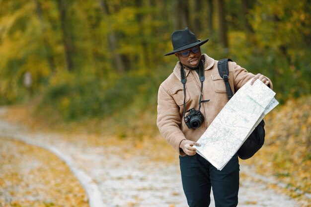 Young black man hitchhiking on road and looking at map. Male traveler feeling lost, traveling alone by autostop