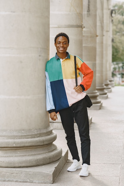 Giovane uomo di colore sorridente in città urbana. ragazzo misto in un maglione colorato.