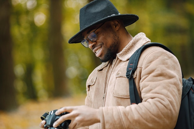 카메라와 함께 숲에도 서 있는 젊은 흑인 남자. 숲에서 산책하는 남성 사진 작가