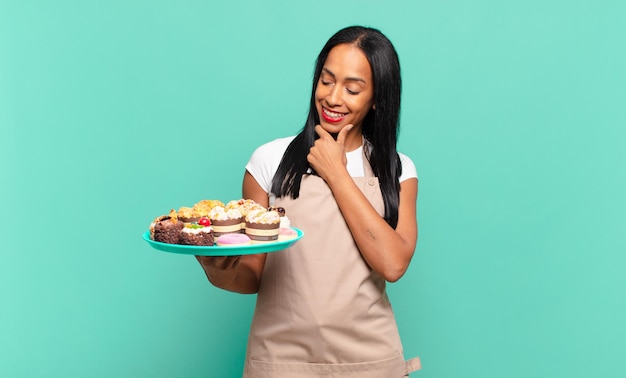 Young black woman smiling with a happy, confident expression with hand on chin, wondering and looking to the side. bakery chef concept