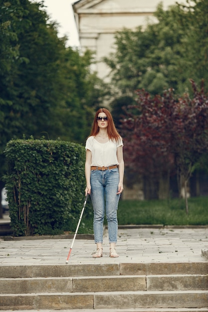 Молодой слепой человек с длинной тростью гуляет по городу