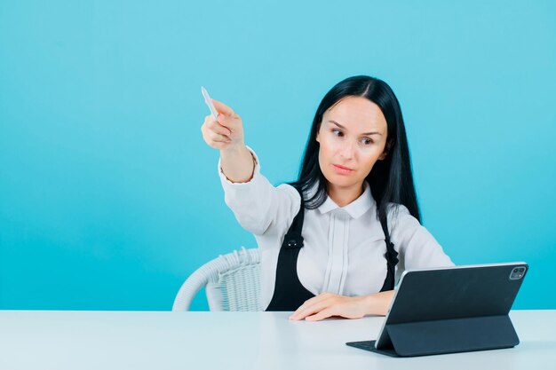 Young blogger girl is looking at tablet camera by pointing away with pencil on blue background