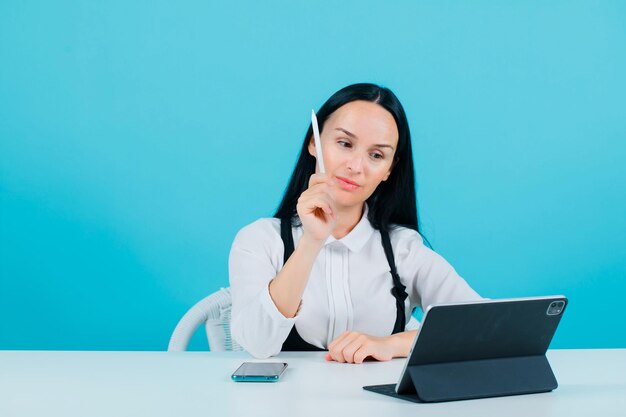 Young blogger girl is showing her pencil to tablet camera on blue background