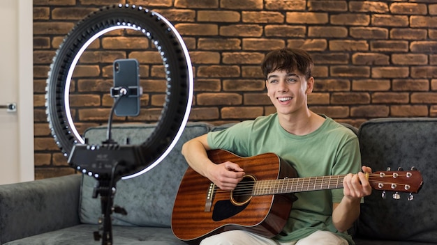 Free photo young blogger influencer shooting himself while playing guitar