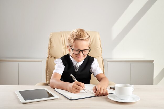 若い白人白人少年のオフィスのエグゼクティブチェアに座って、日記を書く