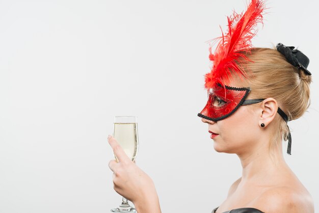 Young blond lady in mask with red feathers holding glass 