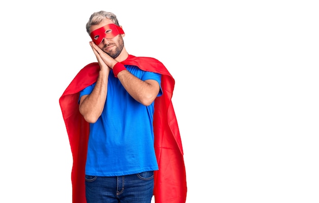 Free photo young blond man wearing super hero custome sleeping tired dreaming and posing with hands together while smiling with closed eyes.