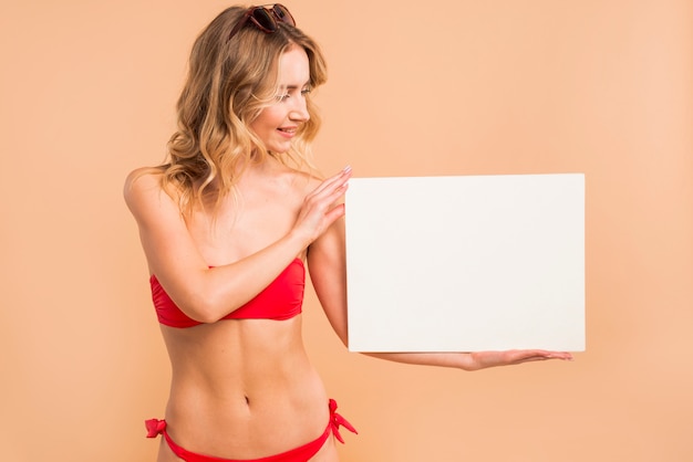 Giovane donna bionda in bikini rosso che tiene scheda vuota