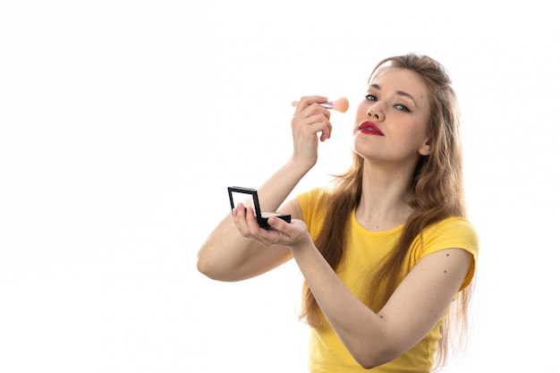 Giovane donna bionda con la maglietta gialla usando il trucco