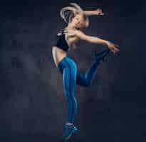 Foto gratuita la giovane ballerina bionda in abiti sportivi balla e salta in uno studio. isolato su uno sfondo scuro.