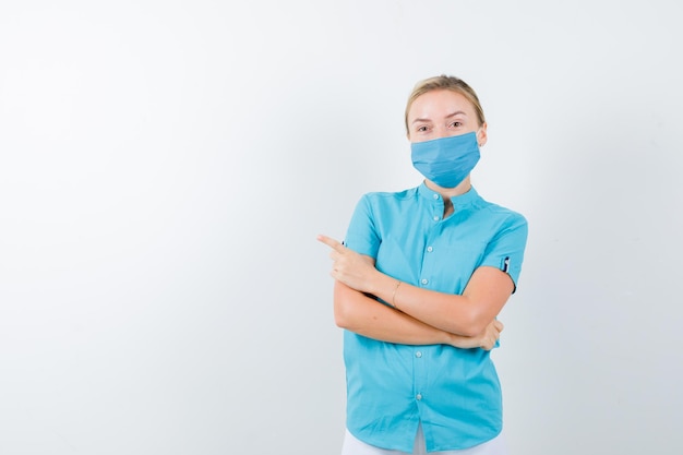 Young blonde female in casual clothes, mask pointing left while holding arms folded