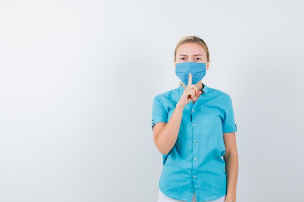 Young blonde female in casual clothes, mask showing silence gesture isolated