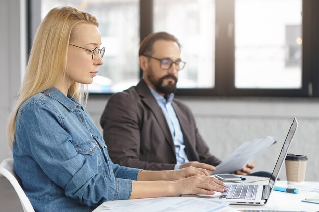 Young blonde female IT developer tests new software application on laptop computer