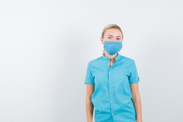 Young blonde female looking at camera in casual clothes, mask and looking pensive