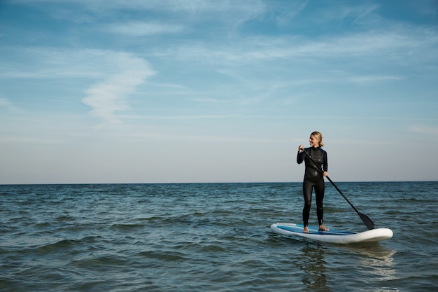 海でパドルボード上の若いブロンドの女性