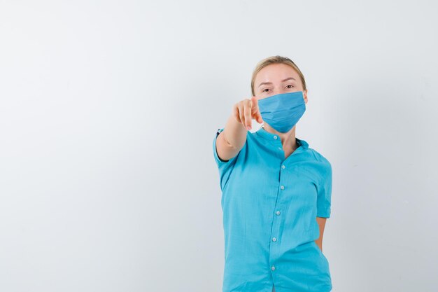 Young blonde female pointing at camera in casual clothes, mask and looking focused