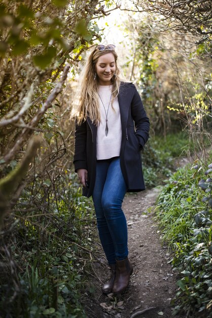 Young blonde female with a black coat standing on a pathway surrounded by leafless trees