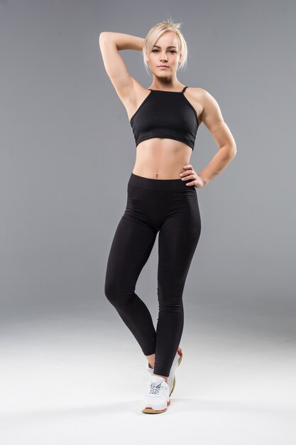 Young blonde fit sporty girl woman in black sportswear demostrate her strong muscular body stretching