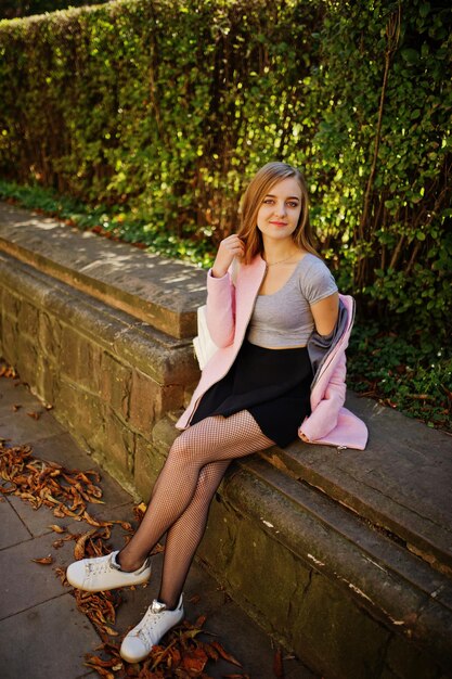 Young blonde girl in black skirt and pink coat posed at sunny day on street