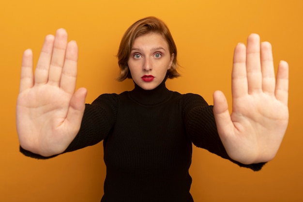 Young blonde girl  doing stop gesture isolated on orange wall