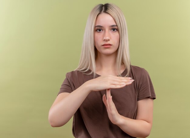 Young blonde girl gesturing timeout on isolated green wall with copy space