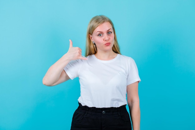 Young blonde girl is looking at camera by showing perfect gesture on blue background