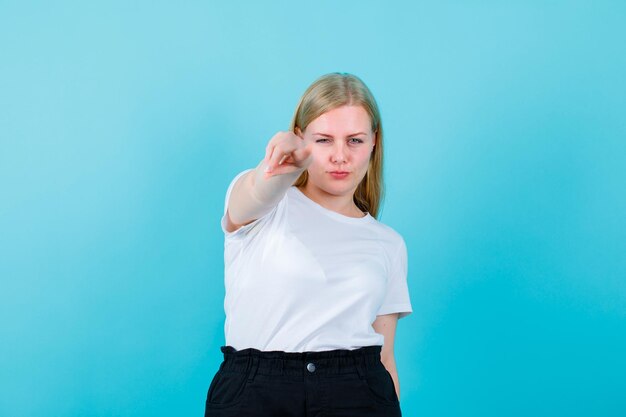 Young blonde girl is showing camera focus with forefinger on blue background