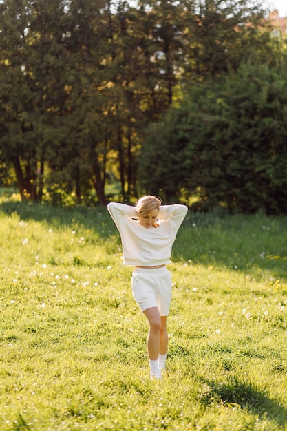 La giovane ragazza bionda indossa una felpa con cappuccio bianca sorridente e cammina nel bosco