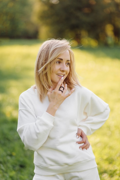 Young blonde girl is wearing a white hoodie smiling and walking in the woods