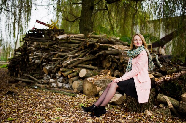 Young blonde girl at pink coat posed against wooden stumps background