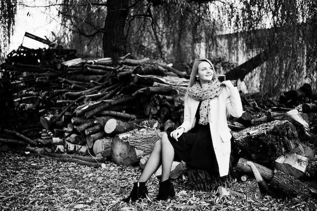 Young blonde girl at pink coat posed against wooden stumps background