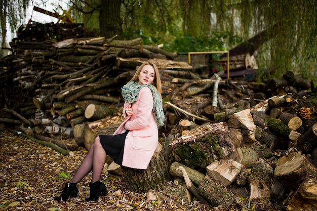 Young blonde girl at pink coat posed against wooden stumps background