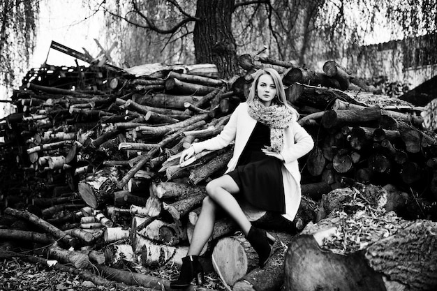 Free photo young blonde girl at pink coat posed against wooden stumps background