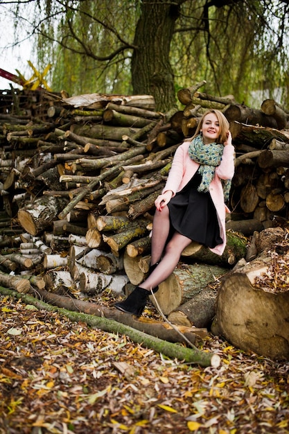 Young blonde girl at pink coat posed against wooden stumps background