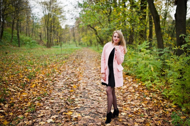 Young blonde girl at pink coat posed on autumn park