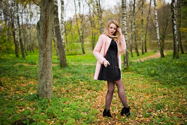 Young blonde girl at pink coat posed on autumn park