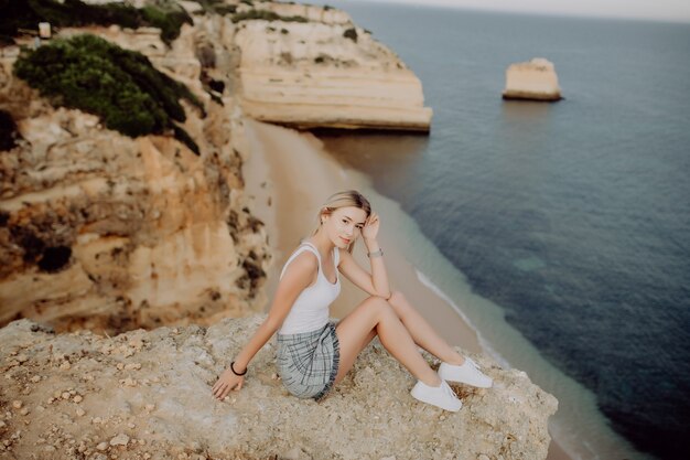 바다를 바라 보는 절벽의 가장자리에 앉아 젊은 금발 소녀.