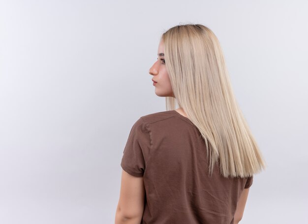 Young blonde girl standing in behind view looking at left side on isolated white wall with copy space