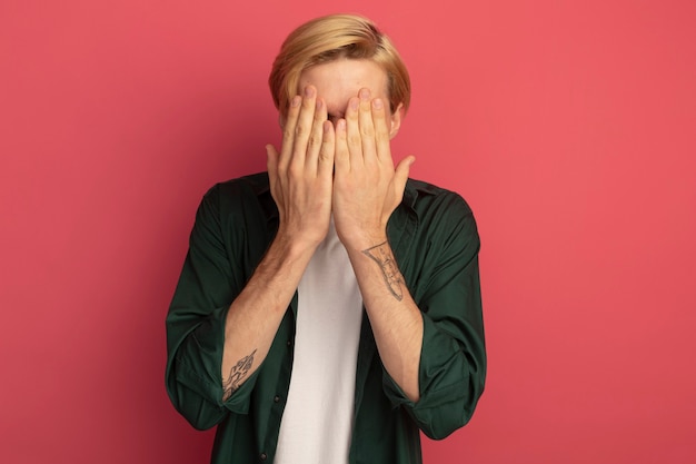 Foto gratuita giovane ragazzo biondo che indossa la faccia coperta di t-shirt verde con le mani