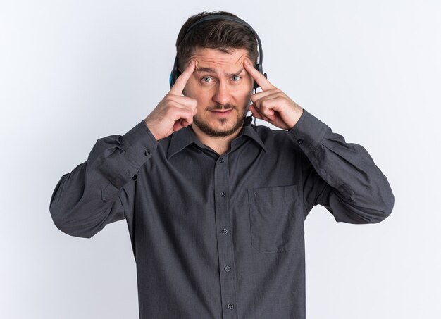 Young blonde handsome man wearing headset raises his eyebrows with hands doing think gesture looking at camera 