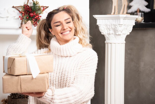 Young blonde lady holding gifts near fireplace. 