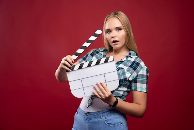 Young blonde model holding a blank movie filming clapper board and having fun.