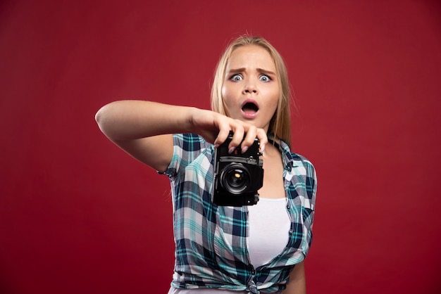 Young blonde photograph holding a professional camera and takes her selfie in strange positions. 