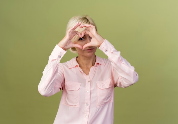 Foto gratuita giovane donna bionda slava che mostra il gesto del cuore isolato su verde oliva