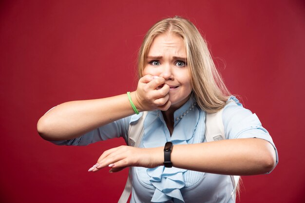 Young blonde student woman goes back to school, checks the time and gets stressed as she is late.