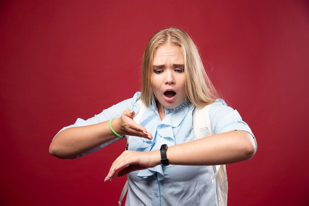 Young blonde student woman goes back to school, checks the time and gets stressed as she is late.