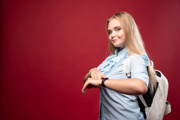 Young blonde student woman goes back to school and checks the time at her watch.